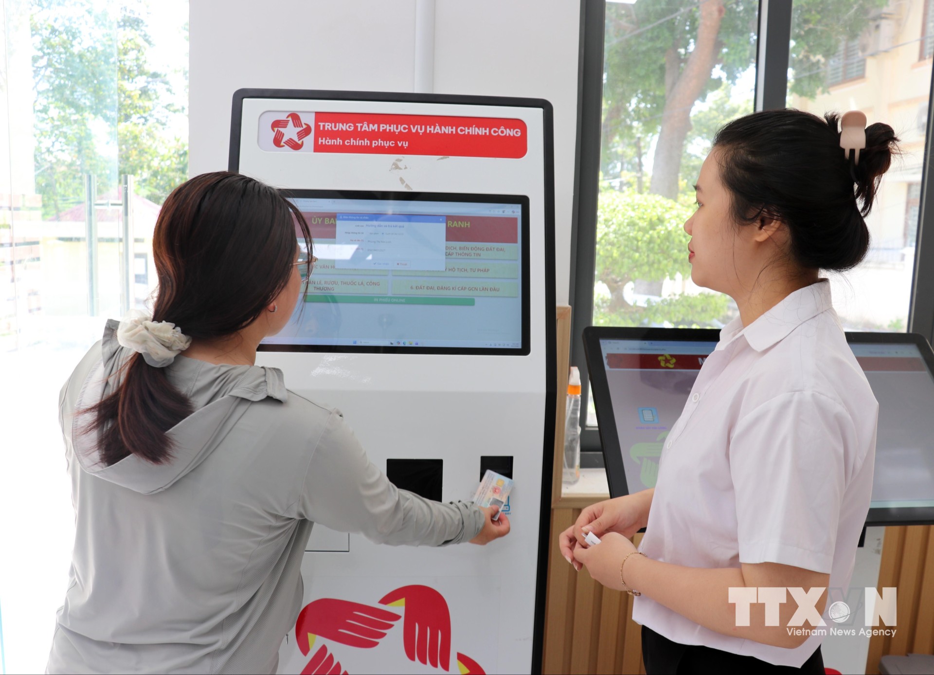 Tư vấn viên của Trung tâm Phục vụ hành chính công phường Cam Ranh hướng dẫn người dân dùng VneID tra cứu thông tin từ robot AL để hỗ trợ các thủ tục hành chính. (Ảnh: Công Thử/TTXVN)